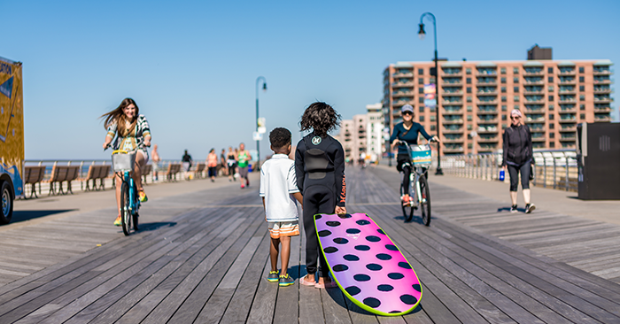 Child with surfboard and people riding bikes on boardwalk